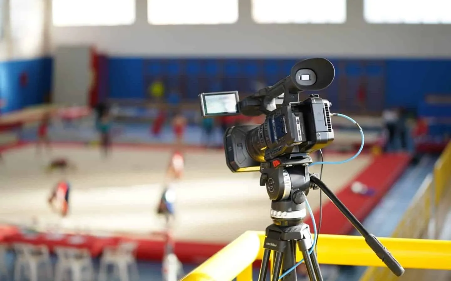 Cámara de vídeo profesional sobre trípode Sachtler enfocando el tapiz de una competición de gimnasia.