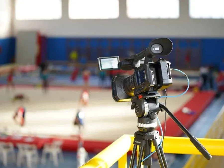 Cámara de vídeo profesional sobre trípode Sachtler enfocando el tapiz de una competición de gimnasia.