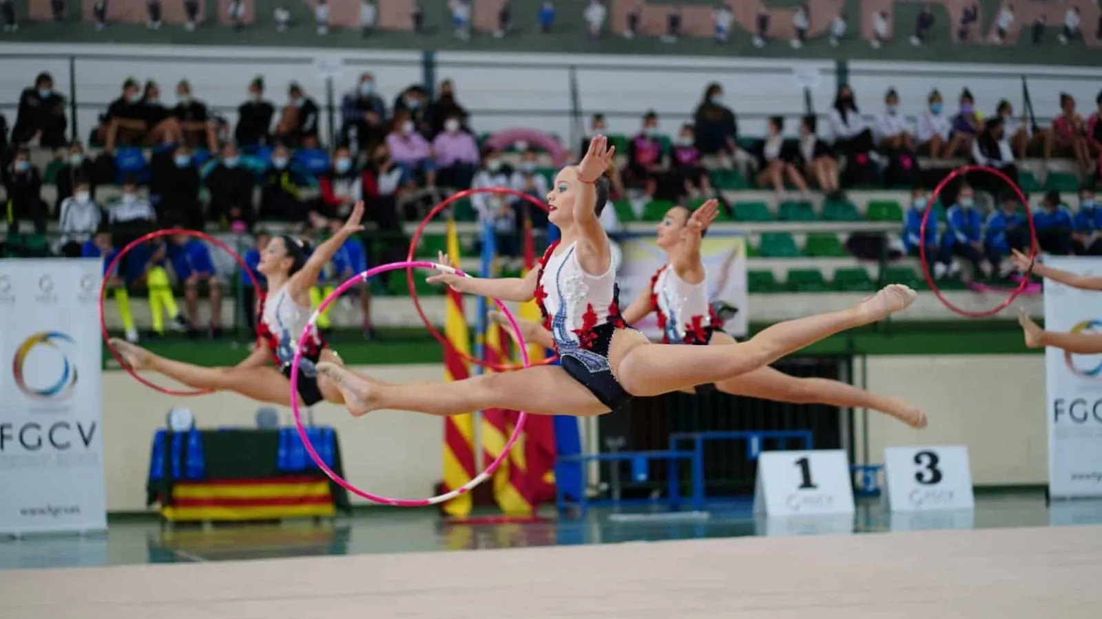 Conjunto de gimnasia rítmica ejecutando un salto simultáneo con aros durante una competición de la Federació de Gimnàstica de la Comunitat Valenciana.