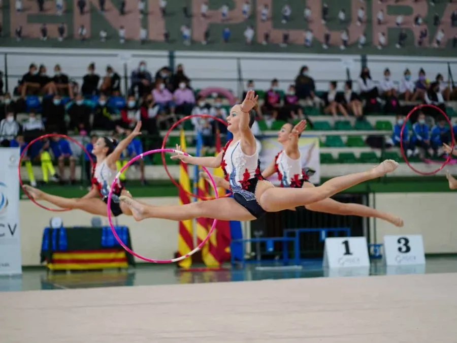 Conjunto de gimnasia rítmica ejecutando un salto simultáneo con aros durante una competición de la Federació de Gimnàstica de la Comunitat Valenciana.
