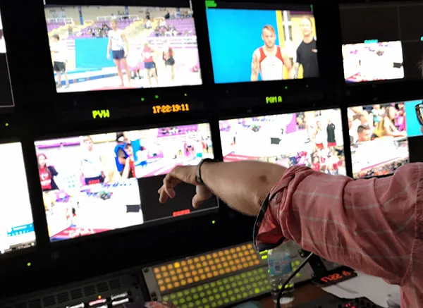 Realizador señalando un monitor del multiviewer con el código de tiempo en pantalla durante un directo de gimnasia.