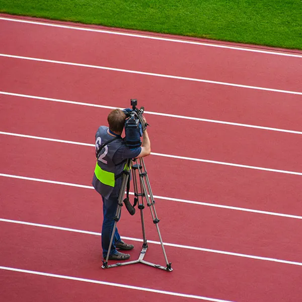 Operador de cámara grabando desde el interior de una instalación deportiva con pista de atletismo.